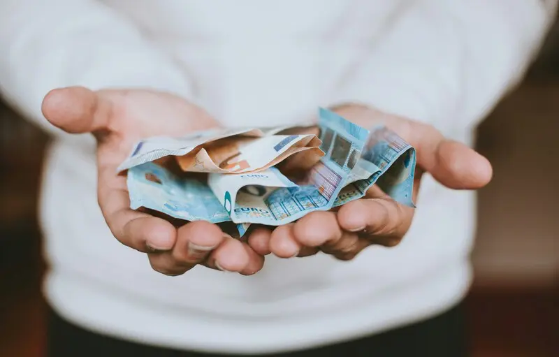 Eine Person hält mehrere zerknitterte Euro-Banknoten in beiden Händen und trägt ein weißes langärmeliges Hemd, das den Wunsch unterstreicht, die Abo-Kosten durch kluge Entscheidungen wie die Verwendung eines Open-Source-Tools zu senken.
